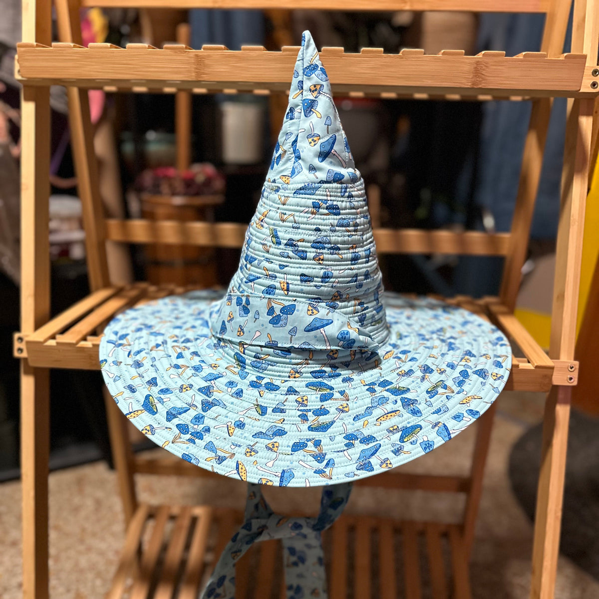 A blue patterned pointed sun hat with a matching wide brim and tie, displayed on a wooden stand.